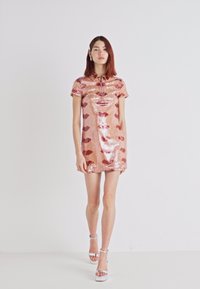 Robe courte en sequins roses avec un col et des manches courtes, arborant un motif de lèvres répété dans des teintes plus sombres. Talons argentés.