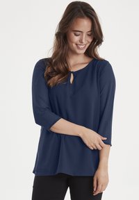 Blusa blu navy con maniche a tre quarti, caratterizzata da un collo a chiave e tessuto leggero e morbido. Taglio casual con una forma fluida.