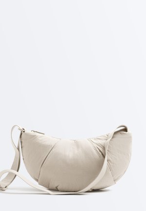Sac épaule rembourré en forme de croissant de couleur beige clair avec une sangle réglable et une fermeture éclair sur un fond uni clair.