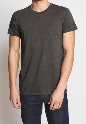 Man wearing a plain dark gray short-sleeve t-shirt and dark blue jeans against a light background.