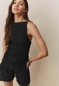 Haut texturé noir avec encolure dégagée, sans manches, et détails froncés, associé à un short texturé noir assorti.