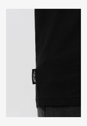 T-shirt in cotone nero con collo a giro, etichetta laterale con la scritta "LEVEL UP" e una texture morbida.