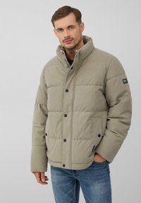 Hellbeige gepolsterte Jacke mit hohem Kragen, schwarzen Druckknöpfen und einem strukturierten Stoff. Verfügt über Seitentaschen und ein Logo-Patch am Ärmel.