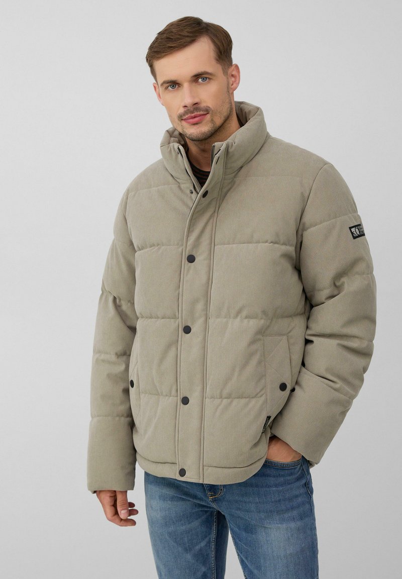 Hellbeige gepolsterte Jacke mit hohem Kragen, schwarzen Druckknöpfen und einem strukturierten Stoff. Verfügt über Seitentaschen und ein Logo-Patch am Ärmel.