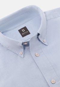 Chemise bleu clair à col classique, en tissu texturé. Comprend quatre boutons blancs et une étiquette noire avec "BOGGI MILANO."