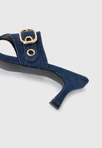Sandale à talons hauts en denim bleu marine, au design élégant, avec une boucle dorée et des œillets, et une semelle en caoutchouc noir.