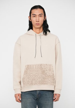 Bees värvi puuvillaseguse materjaliga kapuutsiga sviiter, millel on tekstuuriga mustriga esikott ja mustad nöörid. Sobivad mansetid ja lõdvestunud siluett.