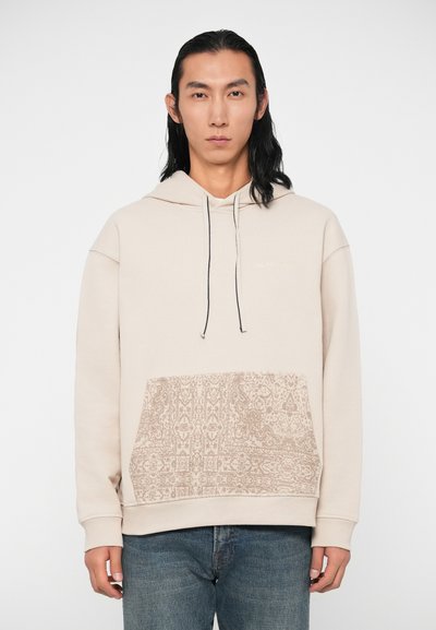 Felpa beige in misto cotone, con una tasca anteriore a motivo testurizzato e cordini neri. Polsini aderenti e silhouette rilassata.