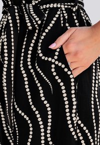 Robe noire avec un motif circulaire blanc. Présente une taille nouée, des poches latérales et une texture lisse. Le design comprend des lignes ondulées de tailles de points variées.