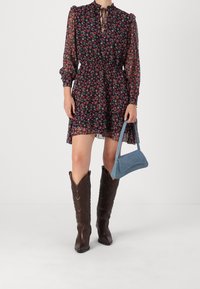 Blommig miniklänning i mörkblått med volangsilhuett, långa ärmar och knytkrage. Matchad med en ljusblå handväska och bruna cowboystövlar.