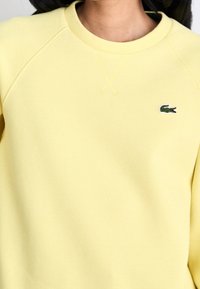 Felpa gialla in cotone texturizzato, con colletto girocollo a costine e logo di un coccodrillo ricamato in verde sul petto.