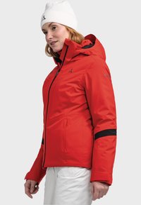 Rote wasserdichte Jacke mit einer taillierten Kapuze, schwarzen Akzenten und mit Reißverschlüssen versehenen Taschen. Glatte Textur mit einem eleganten Design.