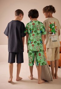 Trois enfants portent différents pyjamas : un t-shirt gris foncé à manches courtes avec un short, un ensemble vert avec motif, et un t-shirt beige avec du texte.