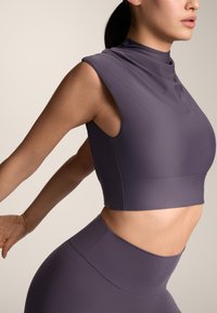 Top attivo viola con collo alto, design senza maniche e silhouette aderente. Texture liscia con una leggera lucentezza.