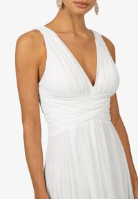 Robe blanche avec un décolleté en V et un froncé au niveau du buste, fabriquée en tissu doux et fluide avec une texture lisse.