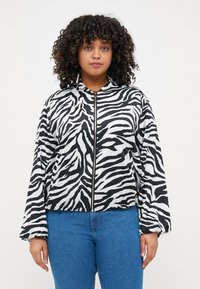 Zebra print takki mustavalkoisena, vetoketjulla edessä, rento istuvuus ja elastiset hihansuut, yhdistettynä sinisiin farkkuihin. Sujuva, kevyt kangas.