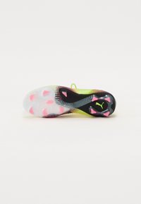 Fotballskoen har en gjennomsiktig gummisåle med rosa og svarte detaljer, en teksturert gul overdel og et mønsterdesign på sidene.