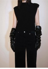 Pull sans manches en tricot noir associé à un pantalon en velours côtelé noir à taille haute et des gants en cuir noir, avec une texture lisse et un design ajusté.