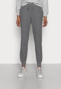 Grijze geribbelde joggers met een elastische tailleband, trekkoord en taps toelopende boorden, gecombineerd met lichtgrijze sneakers.