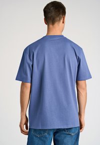 T-shirt in cotone blu con una vestibilità rilassata, maniche corte e colletto rotondo. Tessuto morbido e design semplice, abbinato a jeans in denim blu.