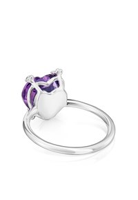 Anillo de plata con una piedra preciosa morada en forma de corazón y corte facetado, sostenida por un engaste detallado. Diseño de banda lisa.