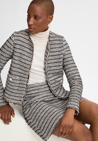 Getextureerde zwart-witte blazer met bijpassende rok, met een opvallend geweven patroon, rafelige randen en voorzakken. Coltrui eronder.