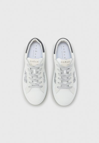 Baskets blanches avec une tige lisse, des accents gris, des détails métalliques sur les côtés et des lacets texturés. Bout arrondi et col rembourré.