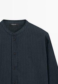 Camicia da uomo blu scuro con bottoni, con sottili righe verticali e colletto rotondo, esposta su uno sfondo bianco.