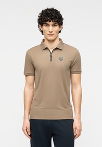 Καφέ πουκάμισο πόλο με κοντά μανίκια, σχεδιασμένο με φερμουάρ και μικρό λογότυπο στο αριστερό στήθος. Λεία υφή και εφαρμοστή σιλουέτα.