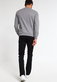 Szary sweatshirt z okrągłym dekoltem, ściągaczami na rękawach i u dołu, w połączeniu z czarnymi dżinsami i białymi sneakersami, widok z tyłu.