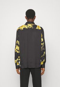 Zwarte langemouwen shirt met een gouden barokpatroon op de schouders en mouwen, met een zachte textuur en een klassieke kraagontwerp.