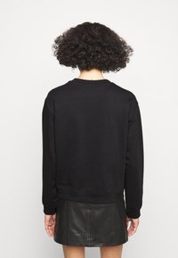 Schwarzer Pullover mit langen Ärmeln, Rundhalsausschnitt und gerippten Bündchen, kombiniert mit einem schwarzen Lederrock. Glatte Textur, keine sichtbaren Muster.