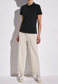 Svart polo skjorta med krage och tre knappar, tillsammans med löst sittande gräddfärgade byxor. Sneakers med ljusgrå och beige detaljer.