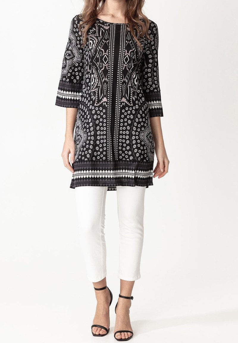 Femme portant une tunique à motifs noir et blanc avec des manches trois quarts, un pantalon blanc court et des talons noirs à bride cheville.