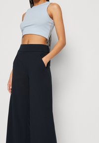Světle modrý bezrukávový crop top spárovaný s vysokým pasem a širokými kalhotami navy, které mají boční kapsy a hladký povrch.