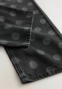 Svart denimtyg med stora, subtila gråa prickar. Har sydda fållar och en mjuk textur som ger ett lager-på-lager, vikta utseende.