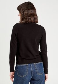 Pull en laine noire à manches longues et bord ribbed, porté avec un jean en denim bleu, affichant un design ajusté et une texture lisse.