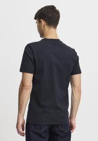 Svart bomull t-skjorte med korte ermer og rund hals. Har en glatt tekstur og avslappet passform, kombinert med mørkeblå jeans.
