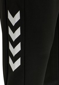 Zwarte sportbroek met een gladde textuur, voorzien van een wit chevronpatroon langs de zijkant voor visueel contrast.