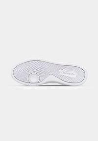 White rubber sneaker sole with textured herringbone pattern, featuring a circular tread design and "Lacoste" logo embossed.