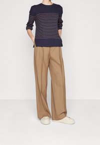 Granatowy sweter w prążki z jasnymi paskami, w połączeniu z beżowymi spodniami o szerokich nogawkach i kremowymi sneakersami. Stylizacja charakteryzuje się luźnym, swobodnym krojem.