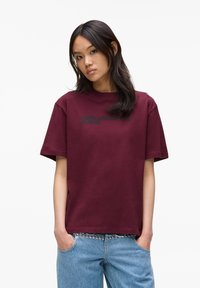 Burgundia puuvillane t-särk ümarate kaelustega, lühikeste varrukatega ja musta "KARL LAGERFELD JEANS" tekstiga, mis on trükitud ette. Kergesti voolav lõige, sile tekstuur.