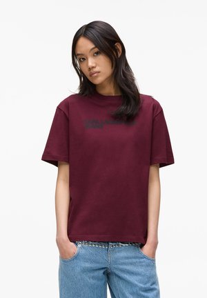 T-shirt en coton bourgogne avec un col rond, des manches courtes, et le texte noir "KARL LAGERFELD JEANS" imprimé à l'avant. Coupe décontractée, texture lisse.