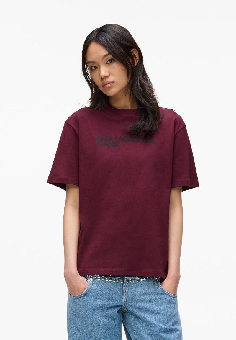 Burgundia puuvillane t-särk ümarate kaelustega, lühikeste varrukatega ja musta "KARL LAGERFELD JEANS" tekstiga, mis on trükitud ette. Kergesti voolav lõige, sile tekstuur.