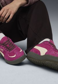 Sneaker in suede rosa con accenti crema, punta rotonda, suola in gomma grigia spessa e lacci marroni. Design della suola testurizzata visibile.
