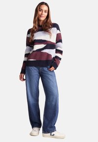 Multicolored fuzzy sweater with bold geometric patterns in navy, burgundy, and cream, paired with loose blue jeans and white sneakers.