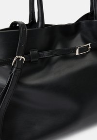 Zwarte leren tote bag heeft een gladde textuur, dubbele handgrepen en een dunne, verstelbare strap met een zilveren gespaccent.