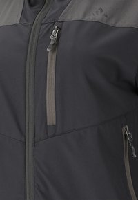 Svart jacka med dragkedja fram, två dragkedjefickor på sidorna och en kontrasterande grå överdel. Tillverkad av ett slätt, lätt material.