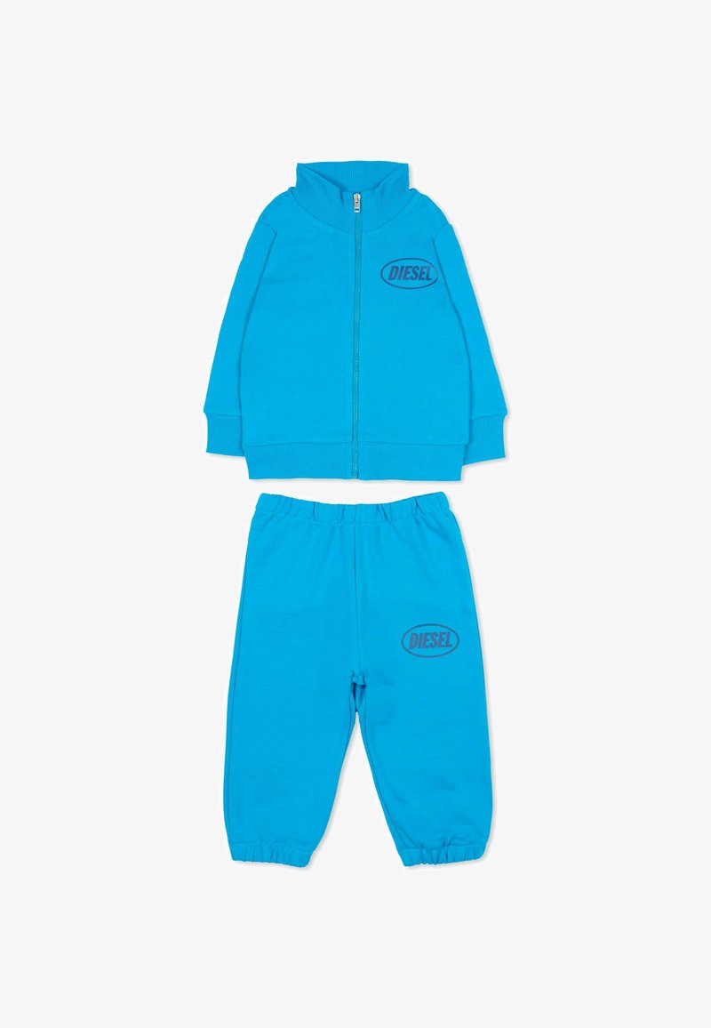 Niebieski dres z miękkiego materiału, składający się z kurtki na zamek z wysokim kołnierzem oraz dopasowanych spodni; oba elementy ozdobione logo "DIESEL".