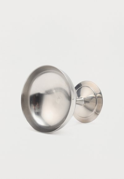 Bleščeč kelih iz nerjavečega jekla z široko skledo in kratkim pecljem, leži na bok na enostavnem belem ozadju.